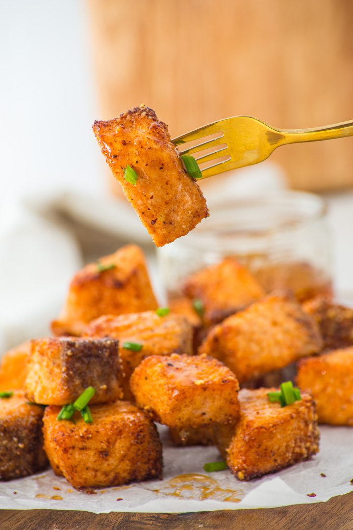 A fork holds a crispy, golden tofu cube above a pile, garnished with chopped green onions—its crunchy coating reminiscent of Air Fryer Parmesan Salmon Bites.