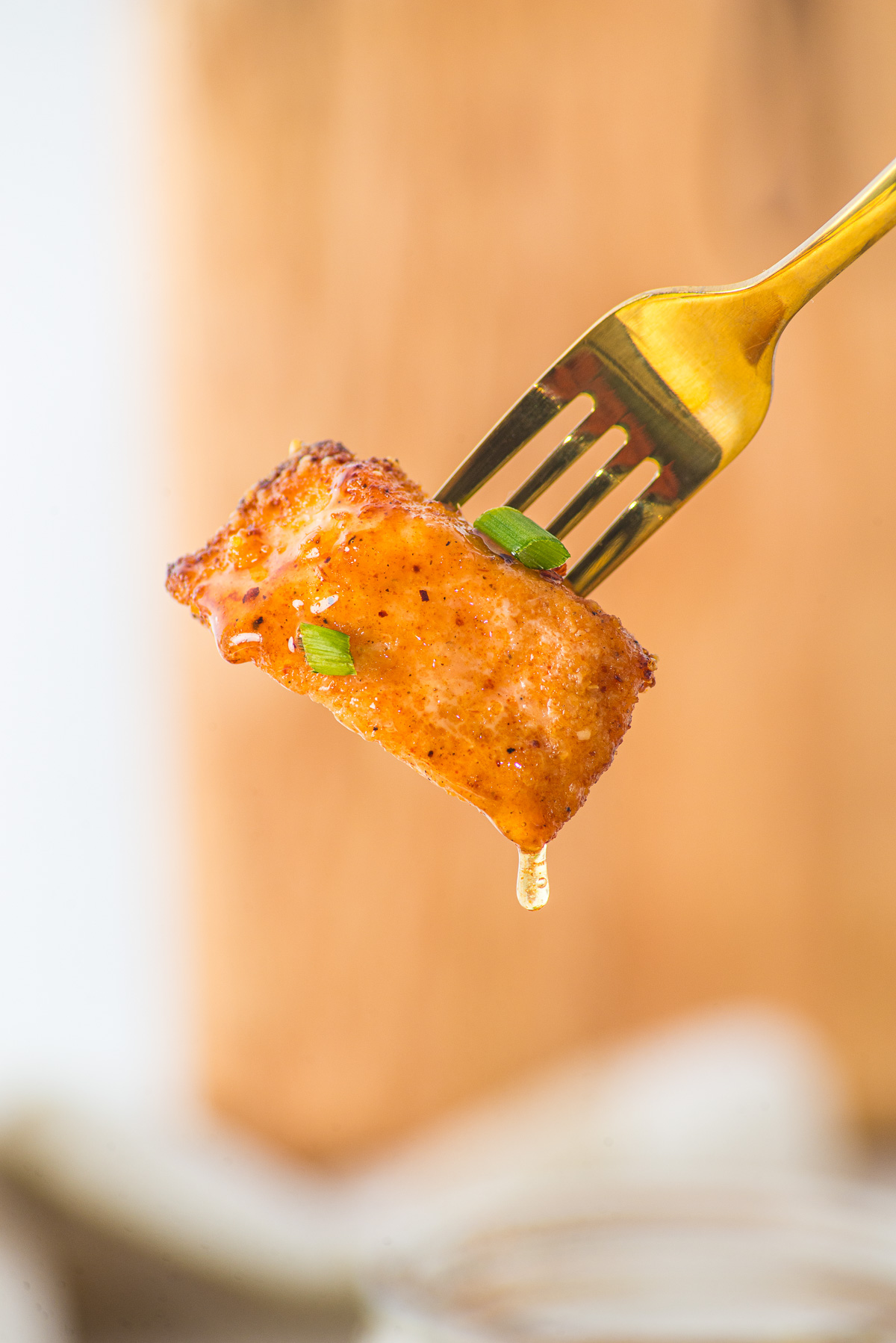A gold fork holds a glazed, seasoned piece of fish—just like Air Fryer Parmesan Salmon Bites—topped with green onions and dripping sauce.