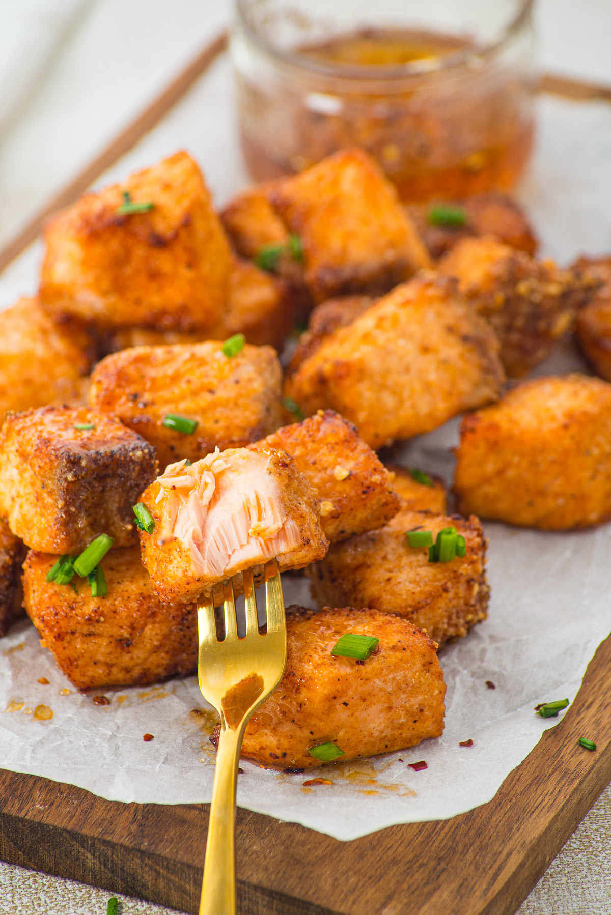 A fork holds a piece of seasoned, cooked salmon atop a pile of similar salmon chunks on parchment paper—these are flavorful Air Fryer Parmesan Salmon Bites, perfectly crisp and ready to enjoy.