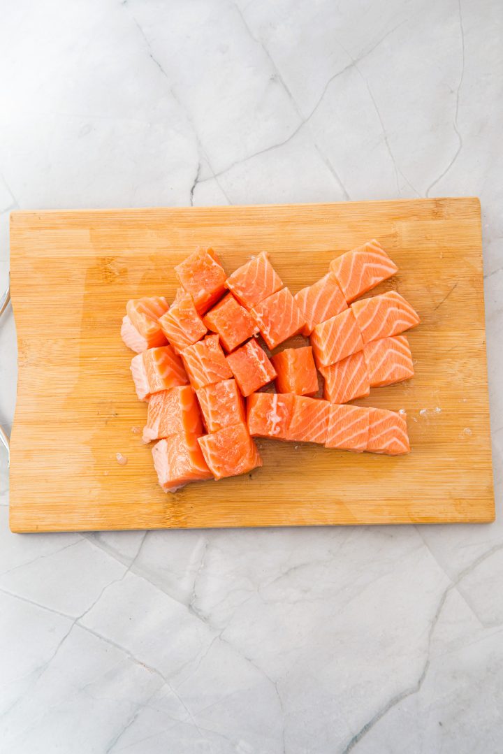 Cubes of raw salmon, perfect for Air Fryer Parmesan Salmon Bites, arranged on a wooden cutting board over a light marble surface.