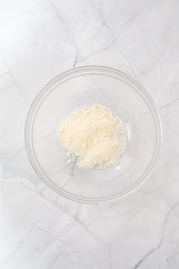 A clear glass bowl with grated parmesan cheese on a white marble surface—perfect for adding the finishing touch to your Air Fryer Parmesan Salmon Bites.