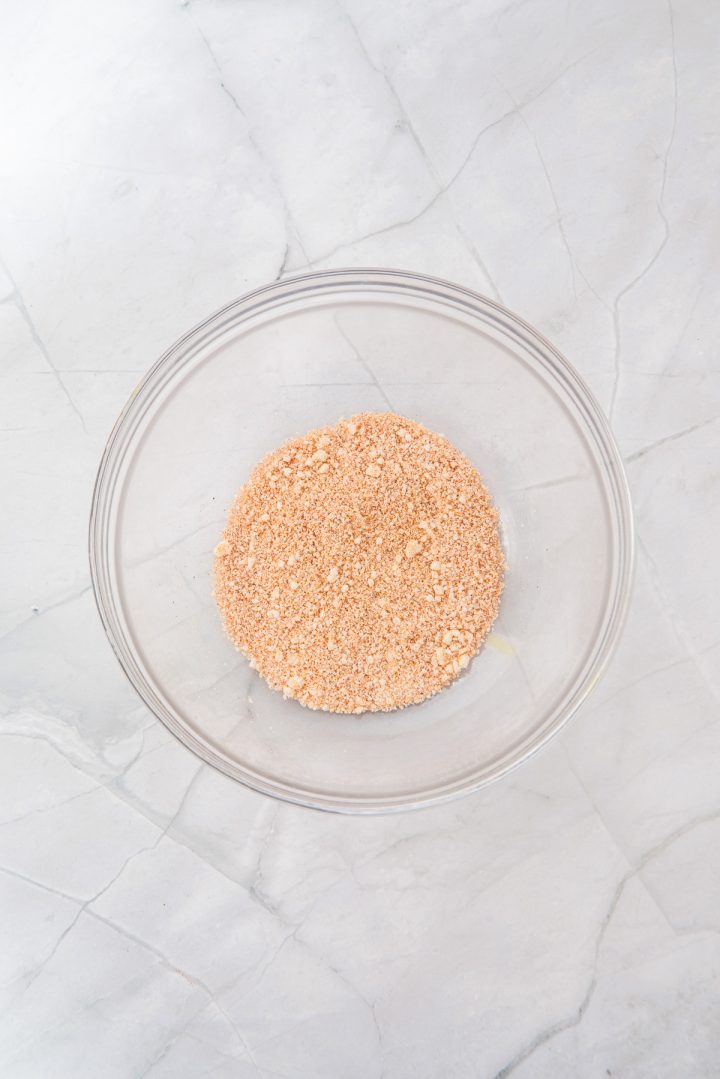A clear glass bowl containing crushed graham crackers on a marble countertop, perfect for preparing toppings or coatings for delicious recipes like Air Fryer Parmesan Salmon Bites.