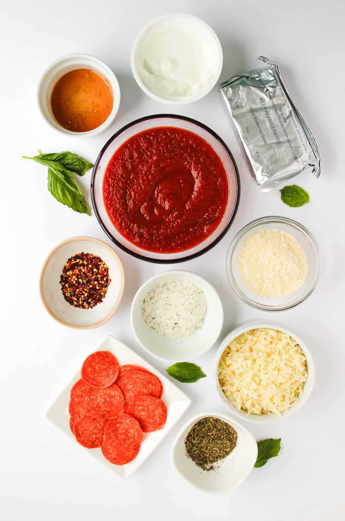 Bowls of pizza ingredients: tomato sauce, cheese, pepperoni, herbs, spices, honey, and cream cheese on white&mdash;perfect for creating a flavorful hot honey pizza dip.