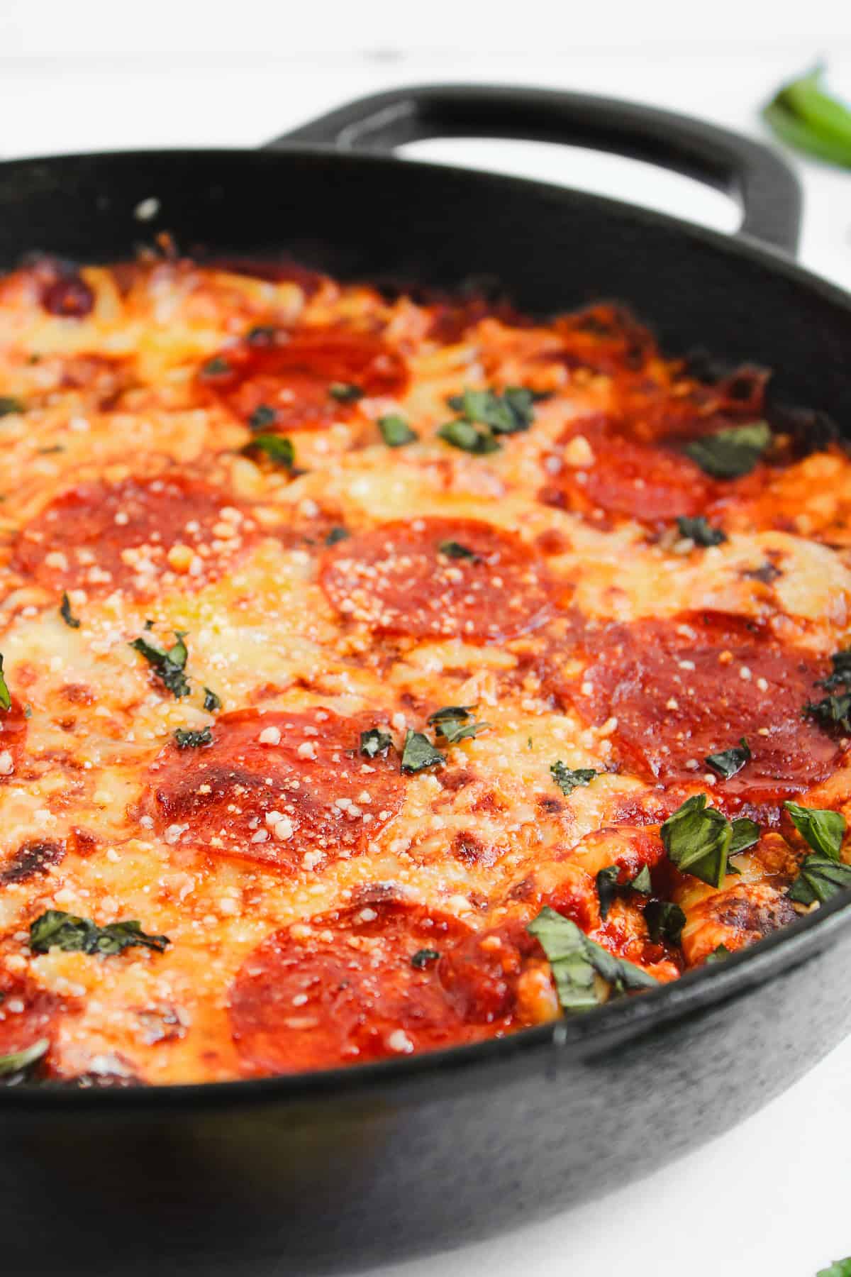 Pepperoni pizza with melted cheese and basil in a black cast iron skillet on a white background, perfect for dipping into a savory hot honey pizza dip.