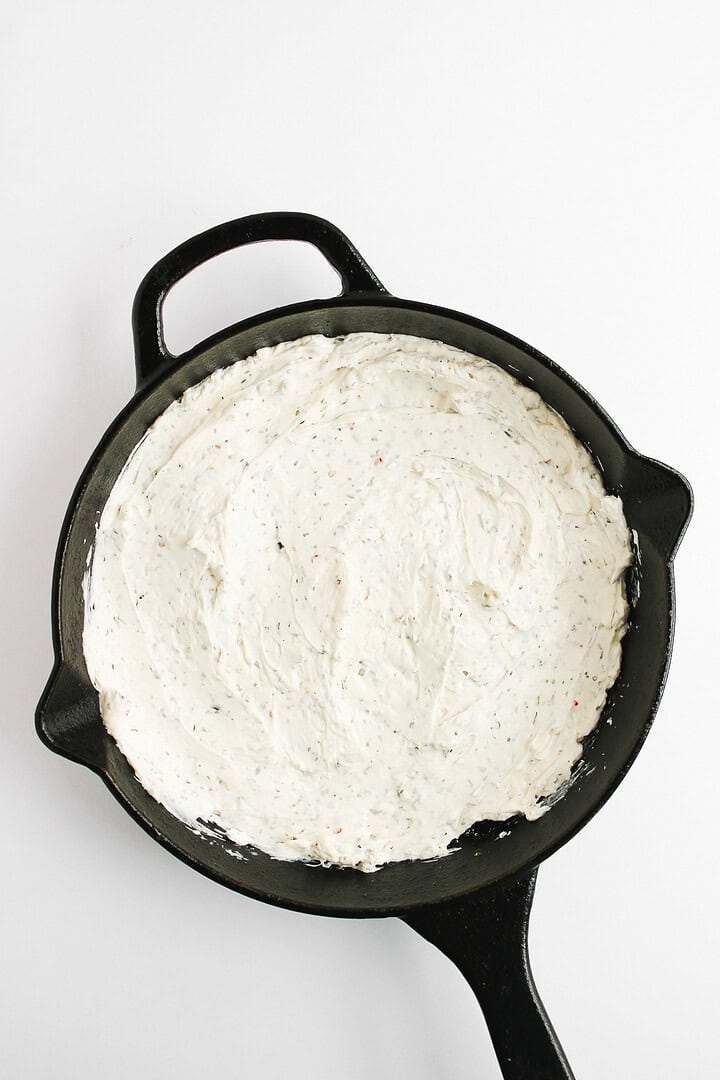 A black skillet filled with a creamy, white, seasoned hot honey pizza dip on a white background.