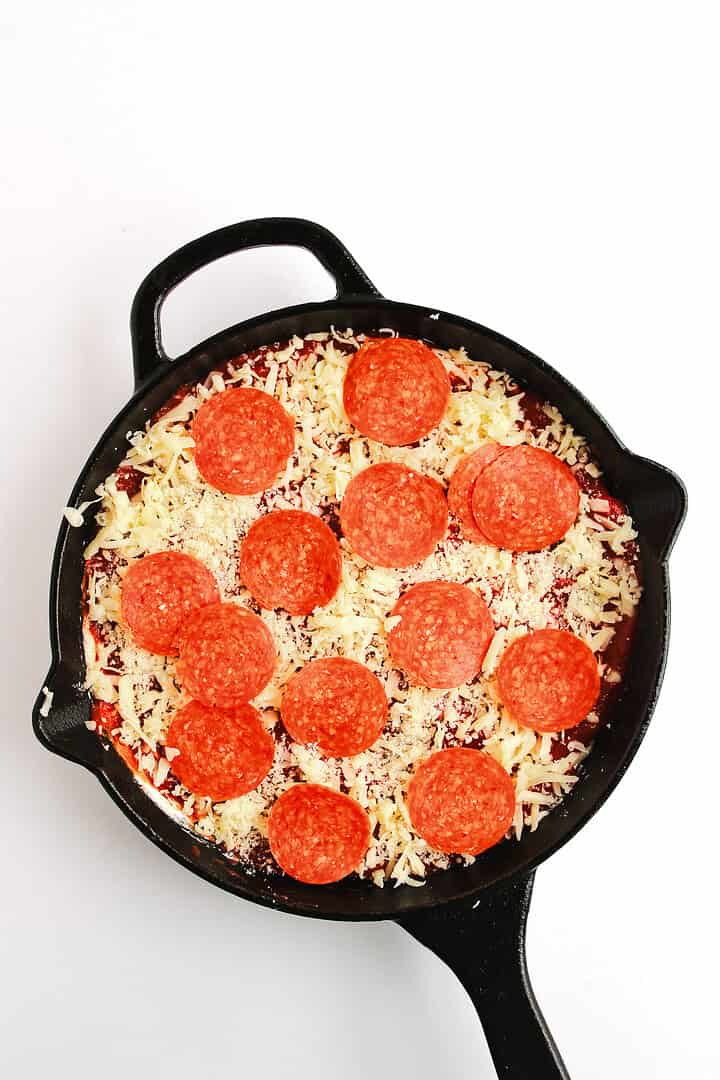A cast iron skillet with an uncooked pepperoni pizza topped with cheese and pepperoni slices, perfect for pairing with a side of hot honey pizza dip.