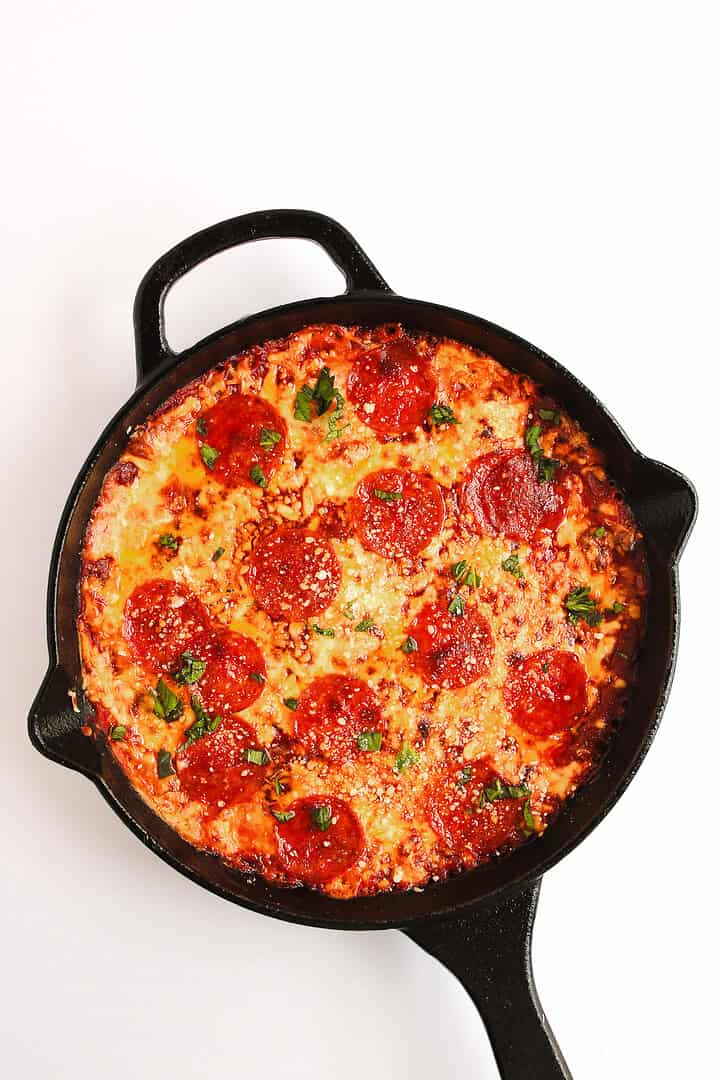 A pepperoni pizza topped with herbs in a black cast iron skillet on a white background, perfect for dipping into hot honey pizza dip.