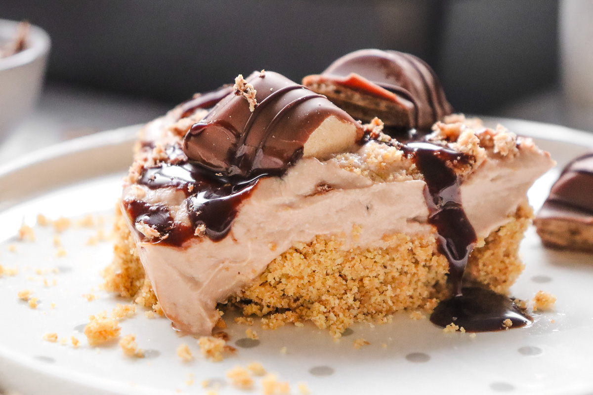 A slice of chocolate cream pie with cookie crust and chocolate drizzle on a white plate, reminiscent of a decadent Kinder Bueno No Bake Cake.