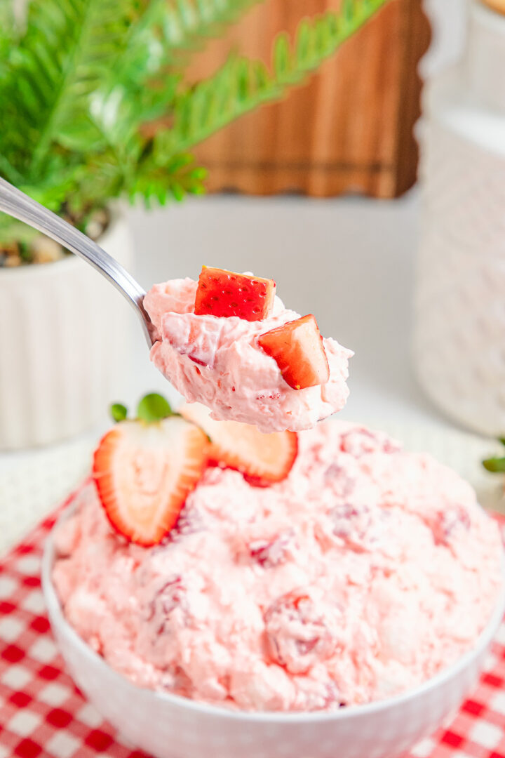 A spoonful of creamy Strawberry Fluff dessert above a bowl, with sliced strawberries on top.