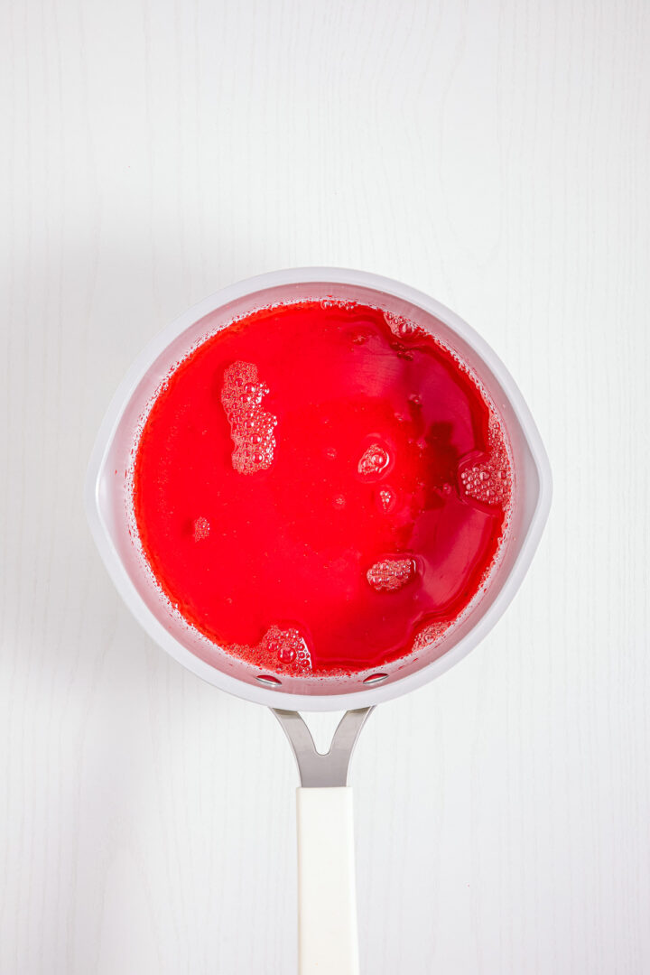 A saucepan filled with bright red Strawberry Fluff sits on a white surface, viewed from above.