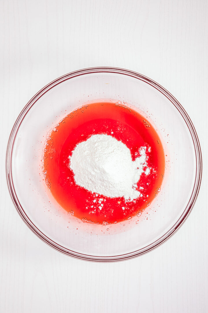 Clear bowl with red liquid and a mound of white powder in the center, on a white surface—perfect for creating your own homemade Strawberry Fluff.