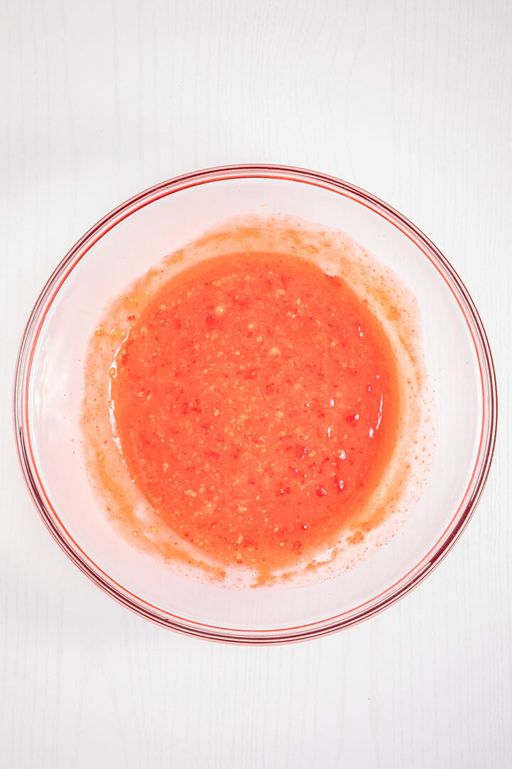 Clear glass bowl with blended bright red strawberry mixture, creating a tempting Strawberry Fluff, on a white surface, seen from above.