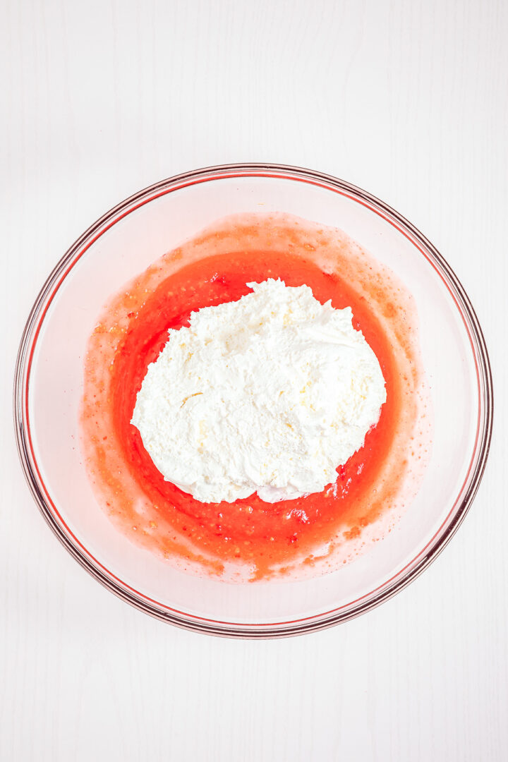 A glass bowl with white ricotta cheese on top of a layer of vibrant red Strawberry Fluff mixture, seen from above.