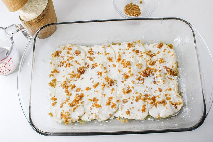 Baking dish with dough covered in white sauce and brown sugar crumbles, ready to be baked into a delightful Strawberry Shortcake Casserole.