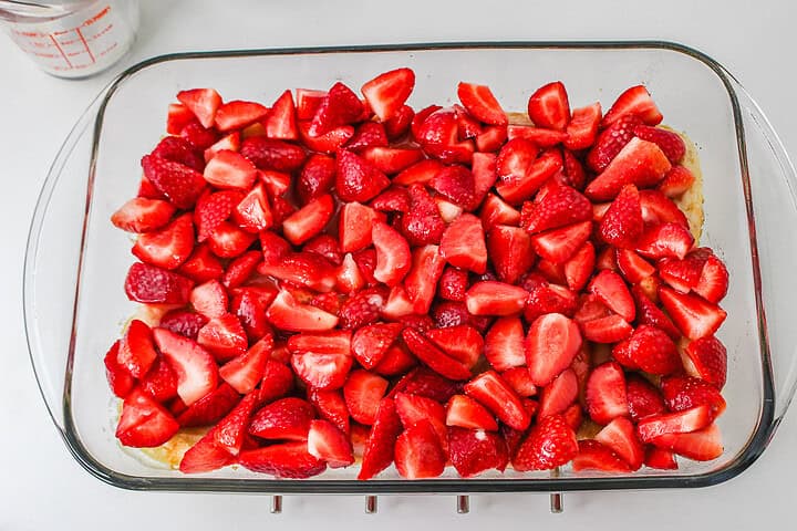 A glass baking dish filled with sliced fresh strawberries on top of an unbaked crust, ready to be baked into a delightful Strawberry Shortcake Casserole.