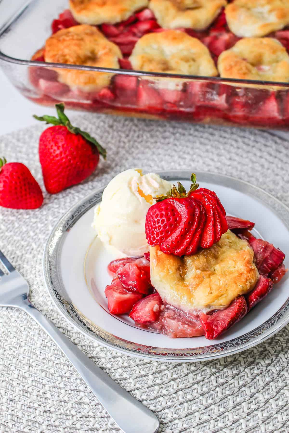 Strawberry cobbler with biscuits and vanilla ice cream, reminiscent of a classic Strawberry Shortcake Casserole, garnished with fresh strawberries on a plate.