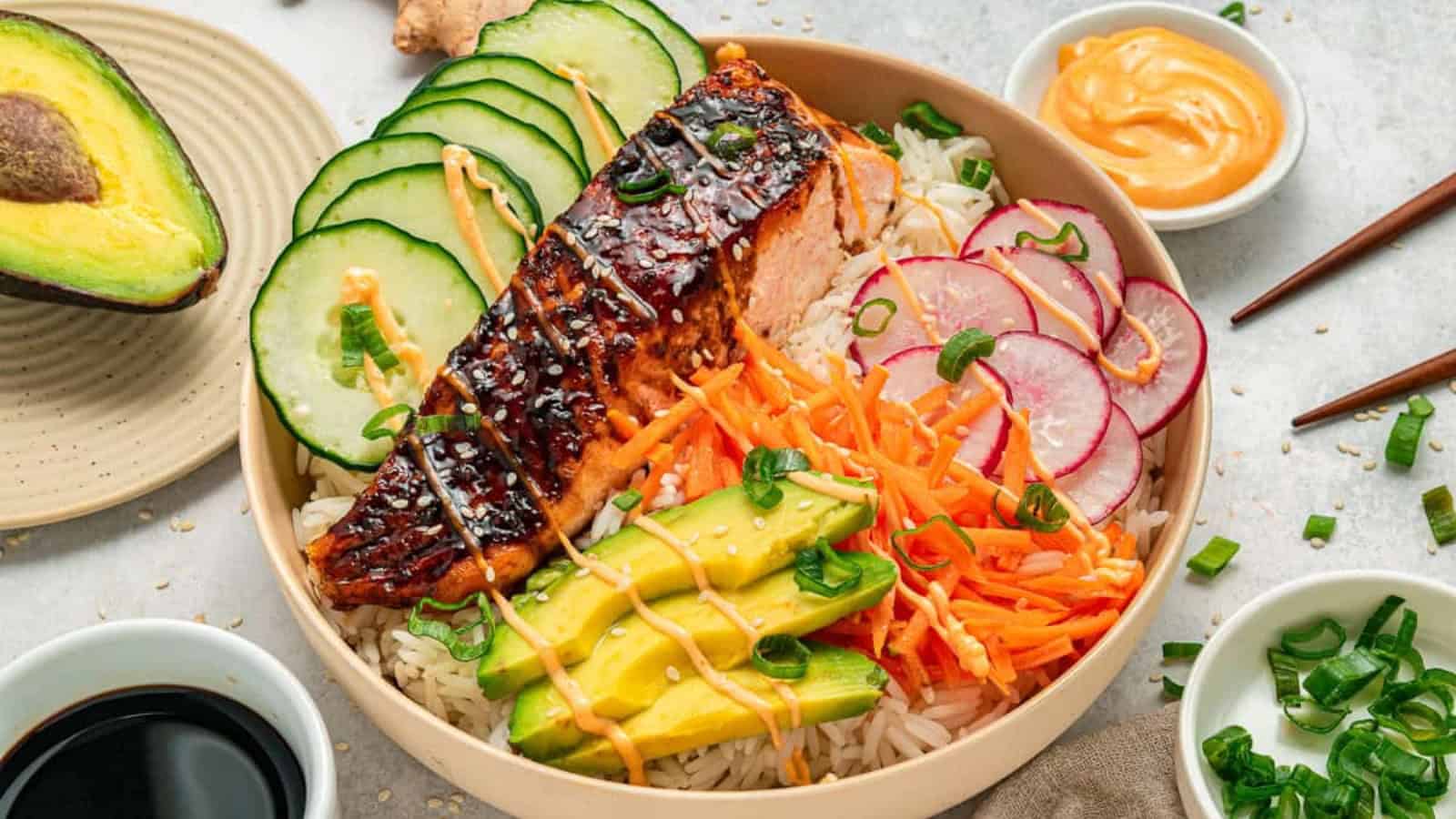 Salmon poke bowl with rice, sliced cucumber, radish, avocado, carrot, and drizzled sauce.