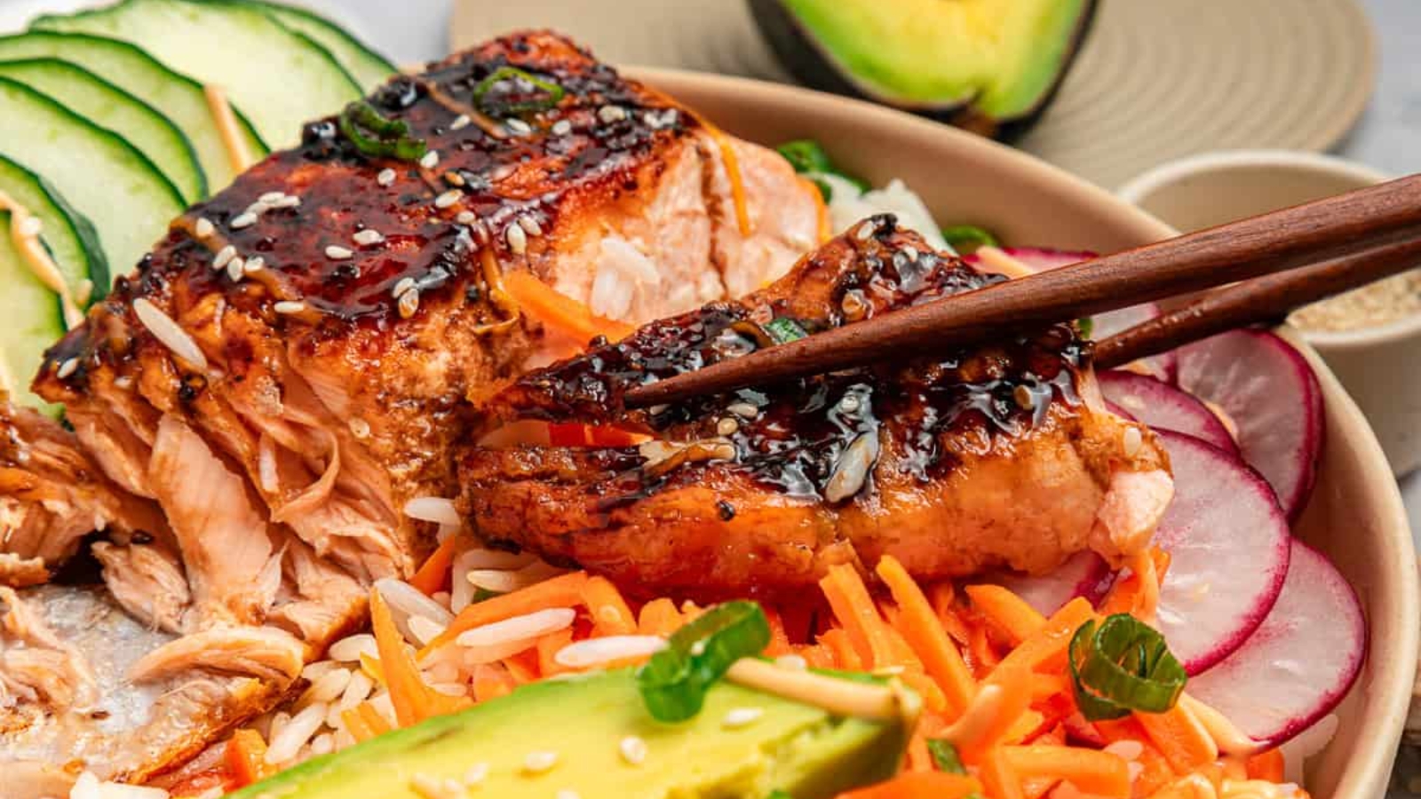 Salmon poke bowl with rice, sliced cucumber, radish, avocado, carrot, and drizzled sauce.