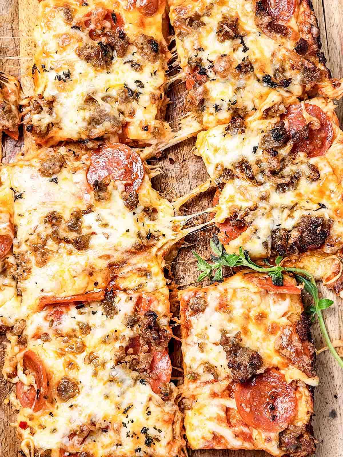 Rectangular slices of Italian Sausage Sheet Pan Pizza topped with pepperoni, sausage, herbs, and melted cheese on a wooden board.