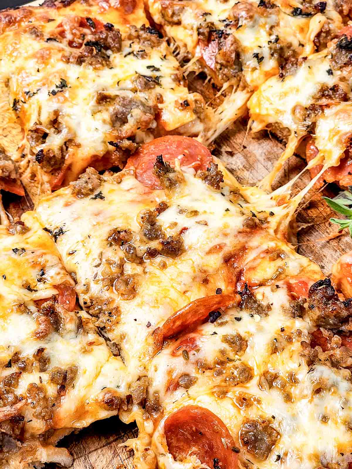 Close-up of cheesy, homemade Italian Sausage Sheet Pan Pizza with pepperoni, cut into square slices on a wooden surface.