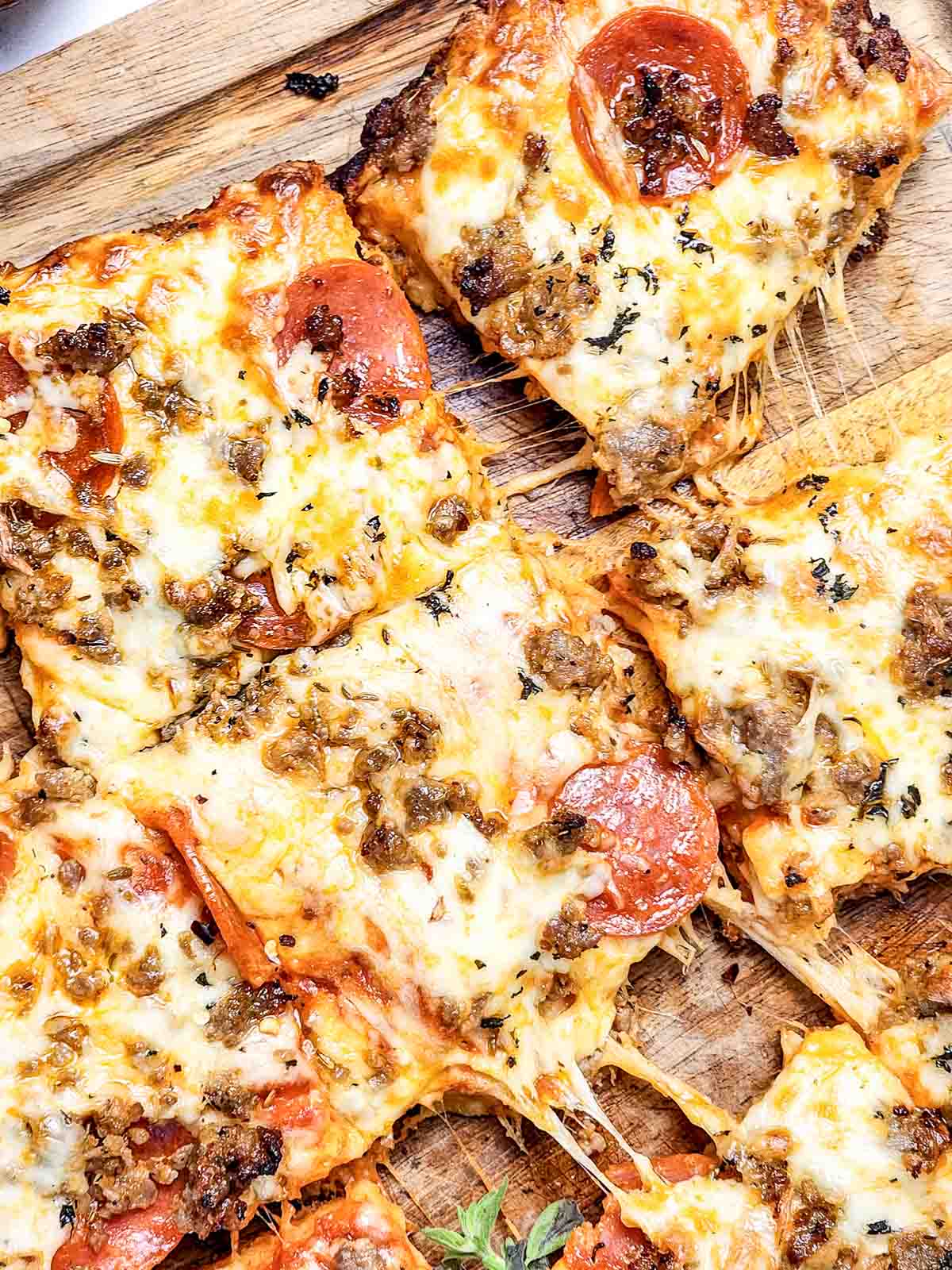 Rectangular slices of cheesy pizza with pepperoni and Italian Sausage Sheet Pan Pizza served on a wooden cutting board.