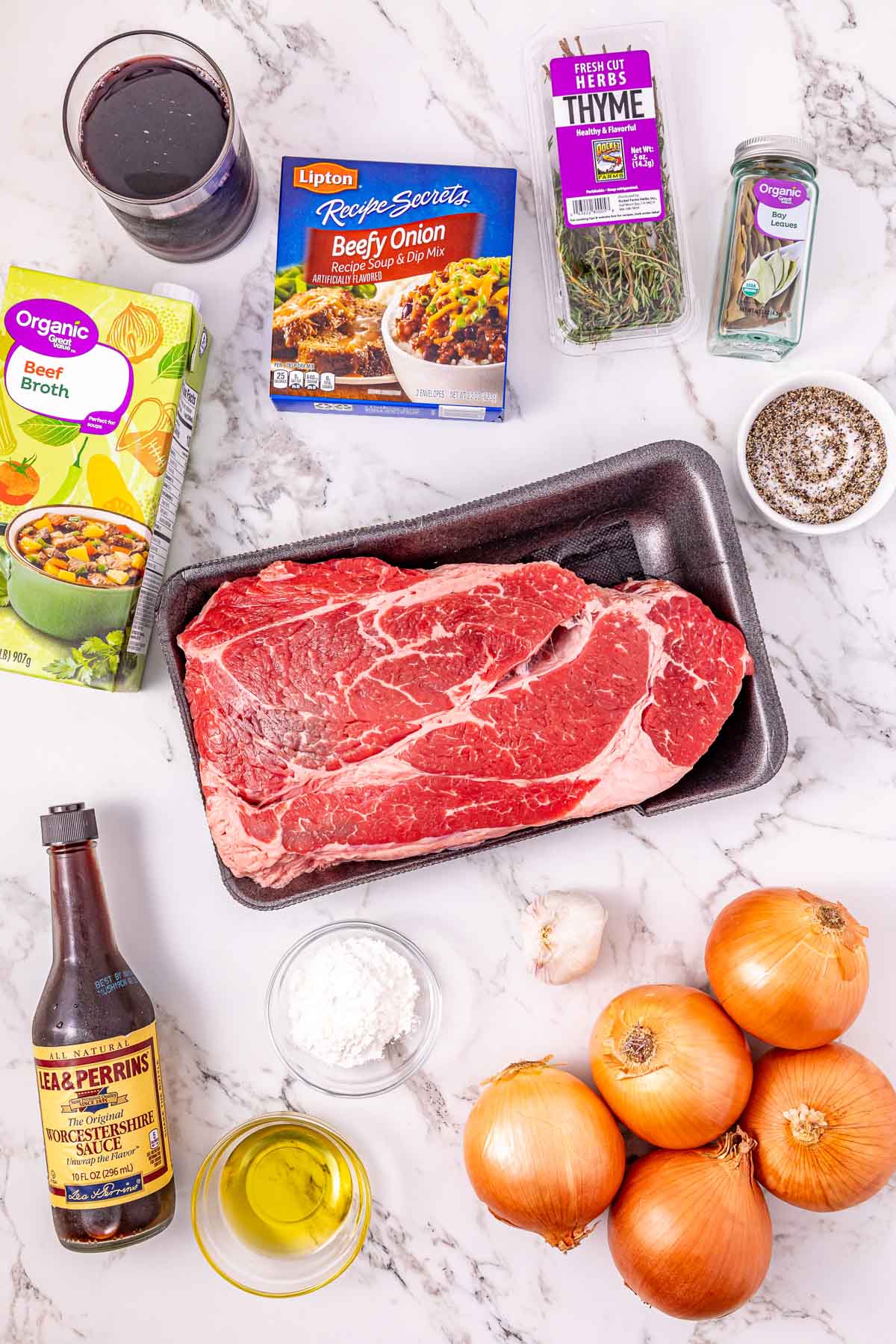 Raw beef, onions, garlic, broth, spices, oil, wine, Worcestershire sauce, and soup mix on a marble surface.