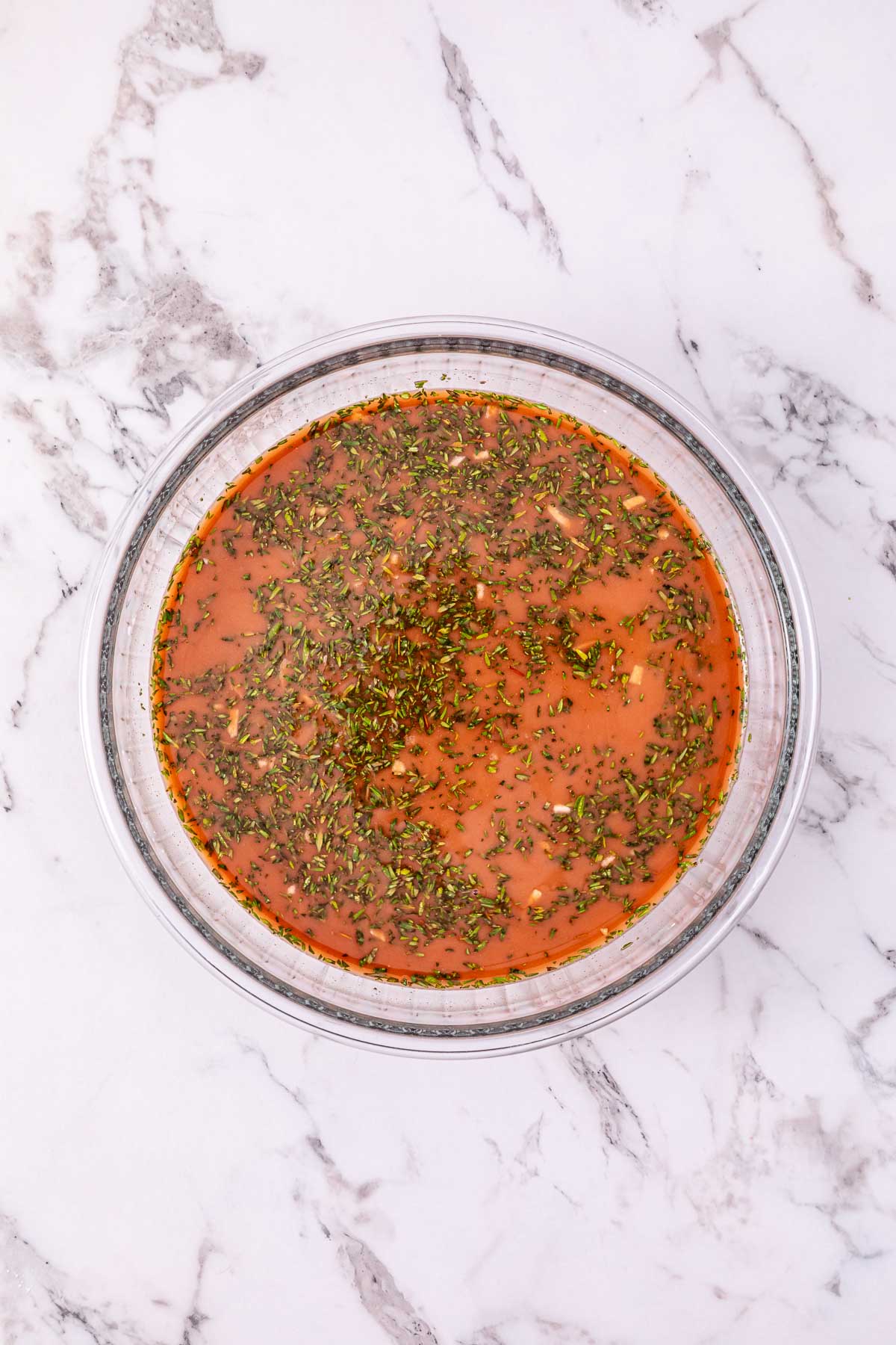 Glass bowl filled with orange-brown liquid and green herbs on a white marble surface, perfect for showcasing the rich broth from a Slow Cooker French Onion Pot Roast.