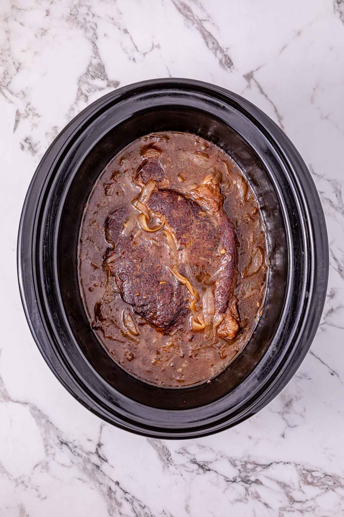 Slow Cooker French Onion Pot Roast with cooked beef roast, onions, and rich gravy on a marble countertop, viewed from above.