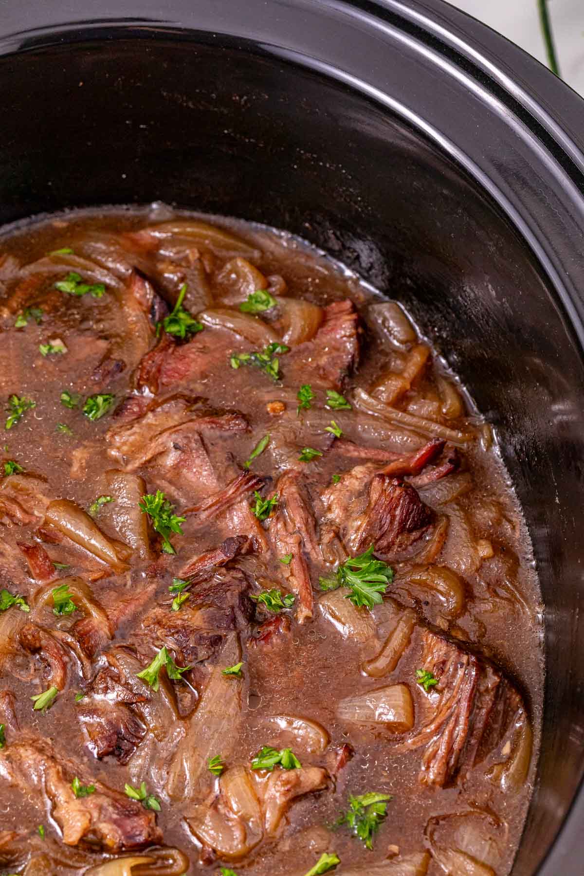 Slow Cooker French Onion Pot Roast with onions and parsley, simmered in a savory brown sauce for a hearty, comforting meal.