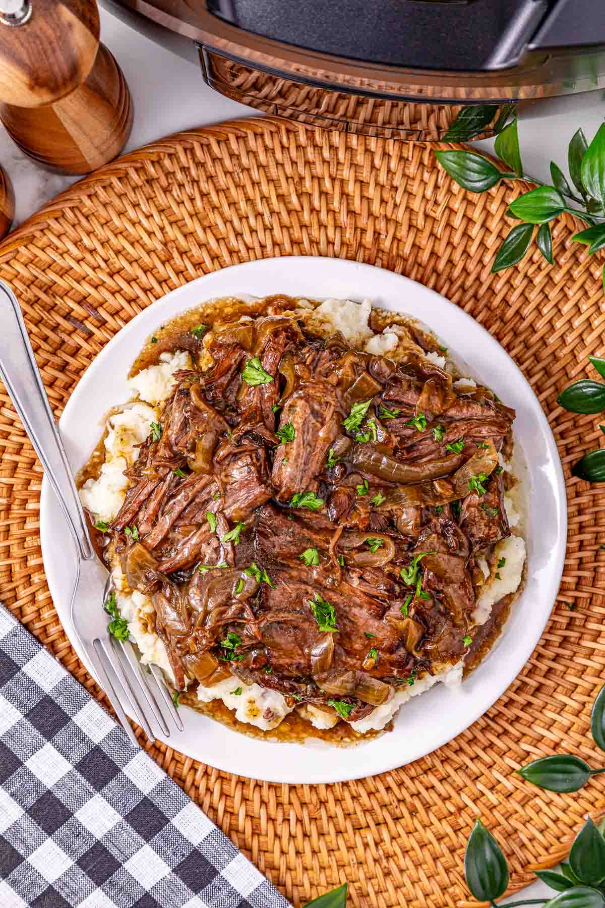 Slow Cooker French Onion Pot Roast shredded beef with rich gravy and caramelized onions is served over creamy mashed potatoes on a white plate, garnished with fresh parsley.