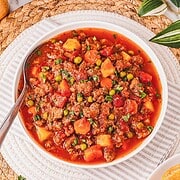 A bowl of Crockpot Poor Man’s Stew with peas, potatoes, and carrots in a rich tomato sauce, garnished with herbs.
