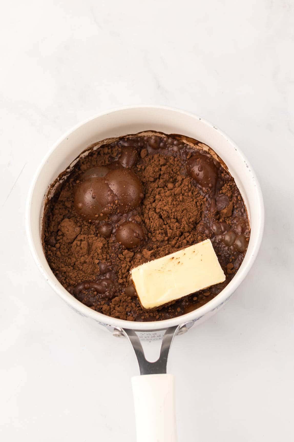 A saucepan with cocoa powder, melted butter, and bubbles on a white surface, ready to be mixed for delicious Dr. Pepper Brownies.