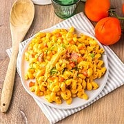 A plate of creamy macaroni pasta with tomatoes and herbs sits on a napkin, next to a wooden spoon and fresh tomatoes, reminiscent of the comforting flavors found in slow cooker cheesy chicken enchilada pasta.