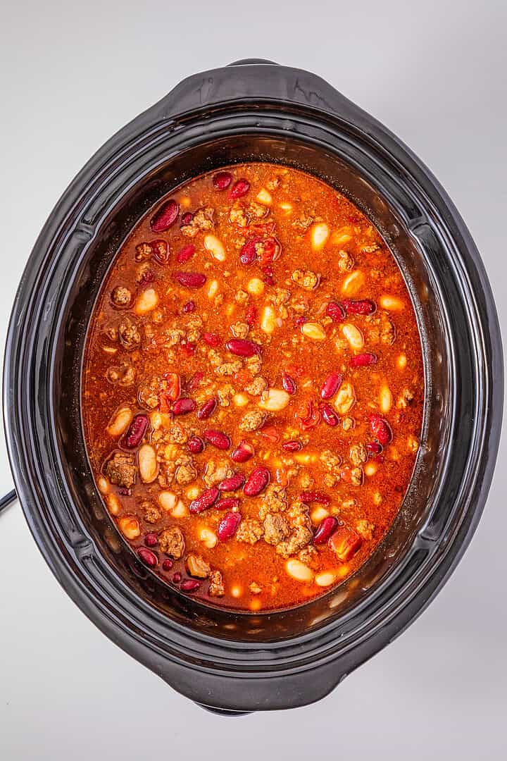 Top view of Slow Cooker Chili with Sausage, beans, and ground meat in a black slow cooker on a white surface.