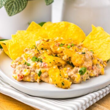 Creamy Slow Cooker Cowboy Dip with corn, peppers, and herbs, served with yellow tortilla chips on a white plate.