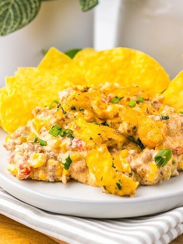 Creamy Slow Cooker Cowboy Dip with corn, peppers, and herbs, served with yellow tortilla chips on a white plate.