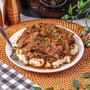 Slow Cooker French Onion Pot Roast features tender braised beef with caramelized onions and rich gravy, served over creamy mashed potatoes and garnished with parsley on a white plate.