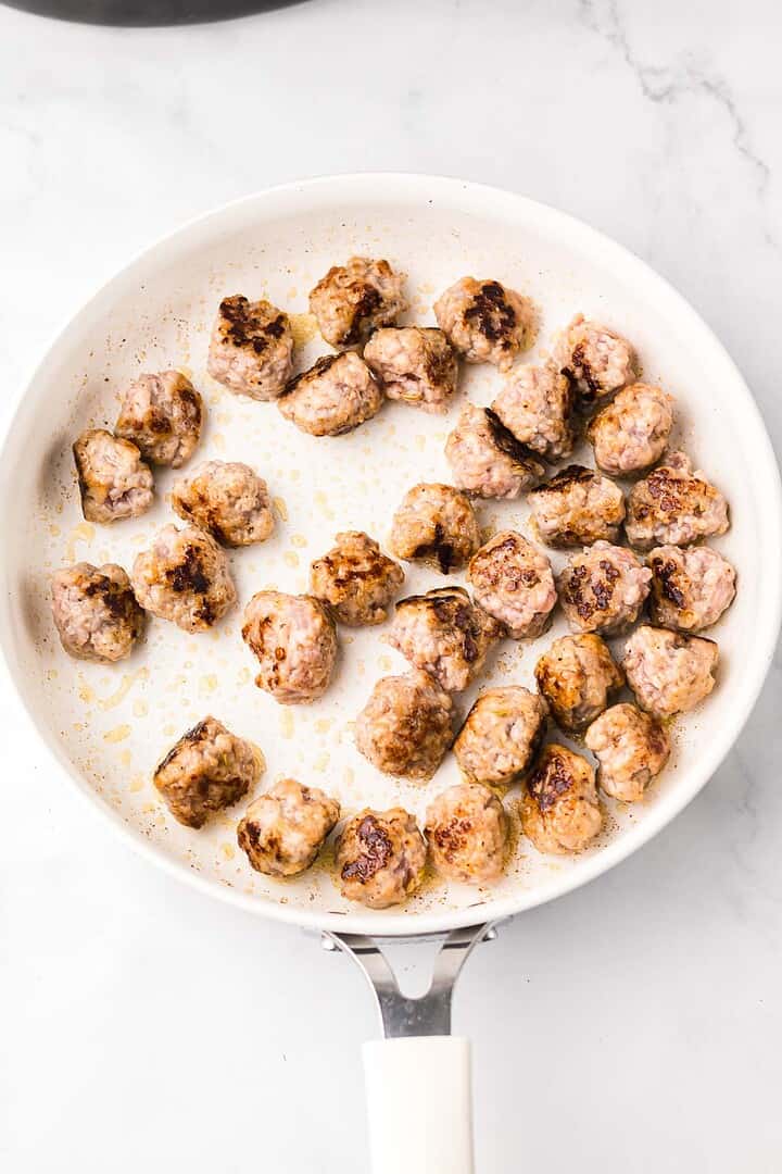 White skillet with browned meatballs cooking on a stovetop, viewed from above on a marble surface—perfectly prepped for adding to your favorite Slow Cooker Italian Wedding Soup.