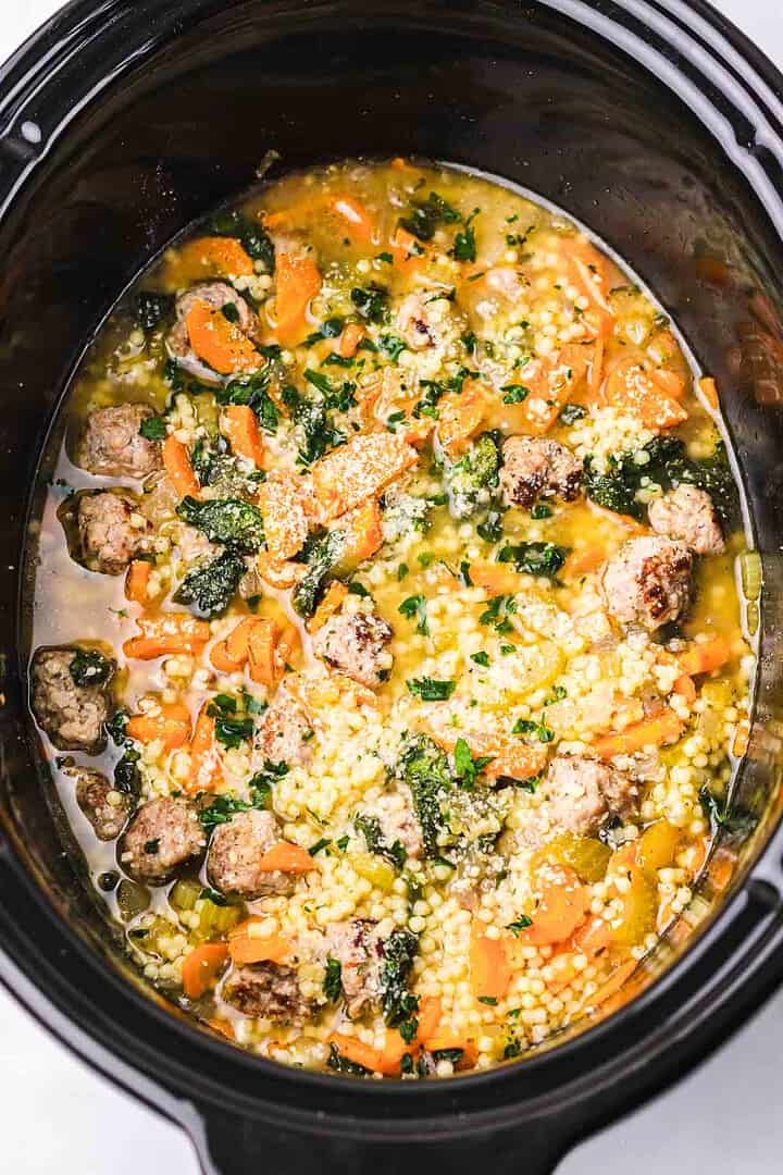 Slow Cooker Italian Wedding Soup with sausage, carrots, spinach, and pasta simmers gently in a black slow cooker, then is topped with fragrant herbs and cheese for a comforting meal.