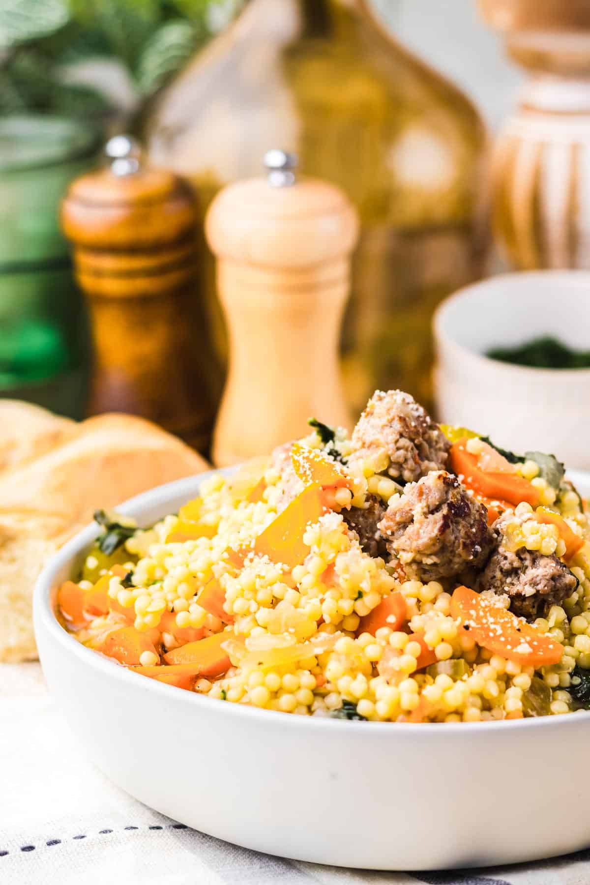 A bowl of couscous with meatballs and vegetables, reminiscent of the comforting flavors found in Slow Cooker Italian Wedding Soup, with salt and pepper shakers in the background.