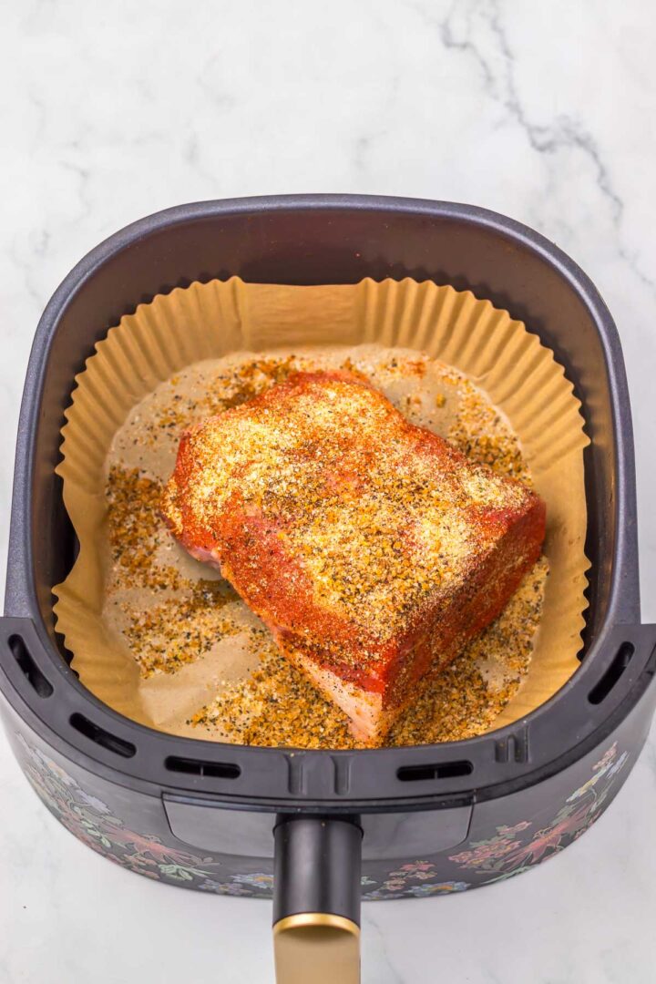 Seasoned Air Fryer Eye of Round Roast sits in a basket lined with parchment paper, ready to cook on a marble surface.