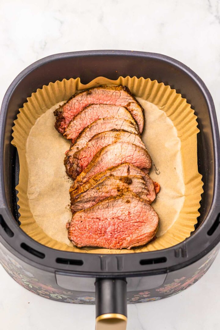 Sliced cooked Air Fryer Eye of Round Roast in an air fryer basket lined with parchment paper.