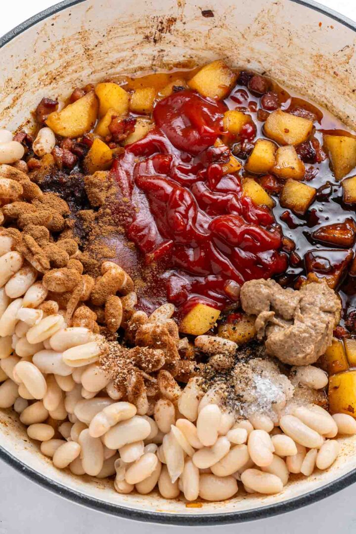 Apple Pie Baked Beans: White beans, chopped apples, ketchup, spices, and sauce mixed in a white pot, ready to be cooked.