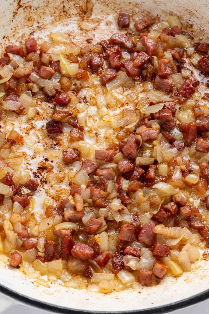 Diced onions and sausage sautéing together in a white pan with browning on the edges, reminiscent of the savory depth found in Apple Pie Baked Beans.