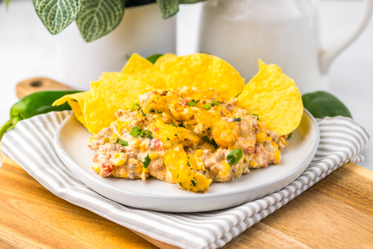 Creamy cheesy Slow Cooker Cowboy Dip with corn, ground meat, and tortilla chips on a white plate with a striped napkin.