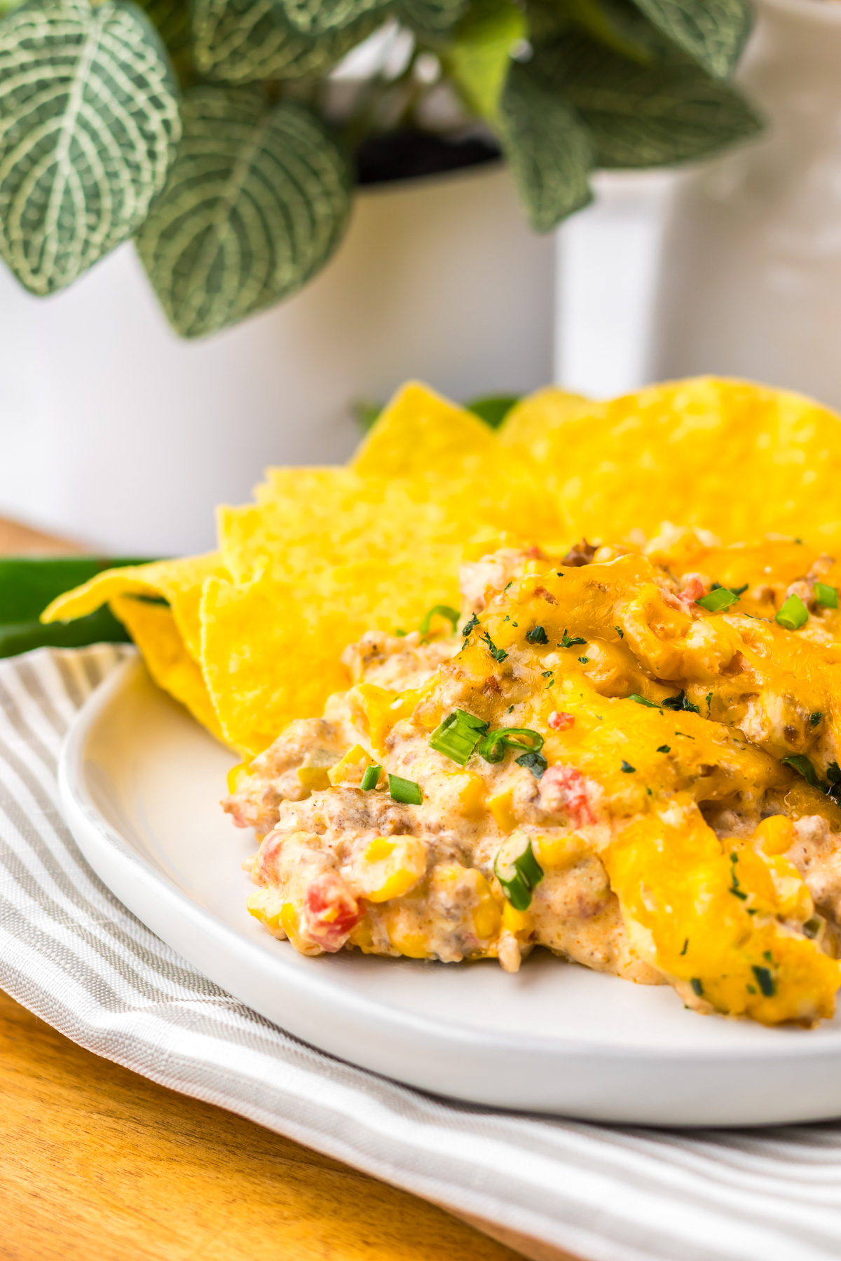 A plate of cheesy casserole with green garnish, served with yellow tortilla chips on the side&mdash;this dish is inspired by the hearty flavors of Slow Cooker Cowboy Dip.