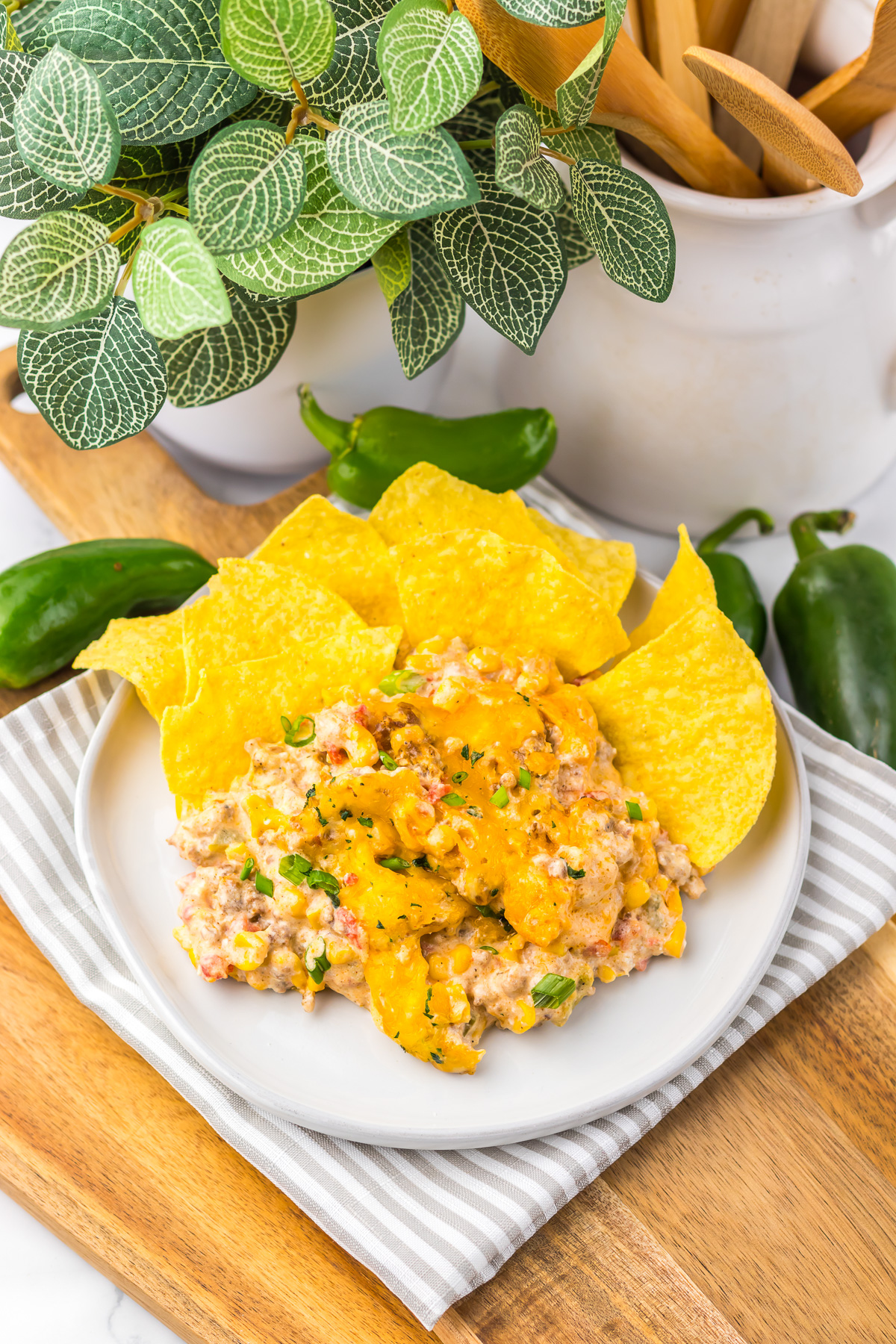 A plate of cheesy Slow Cooker Cowboy Dip topped with herbs, served with tortilla chips, on a wooden tray with peppers nearby.