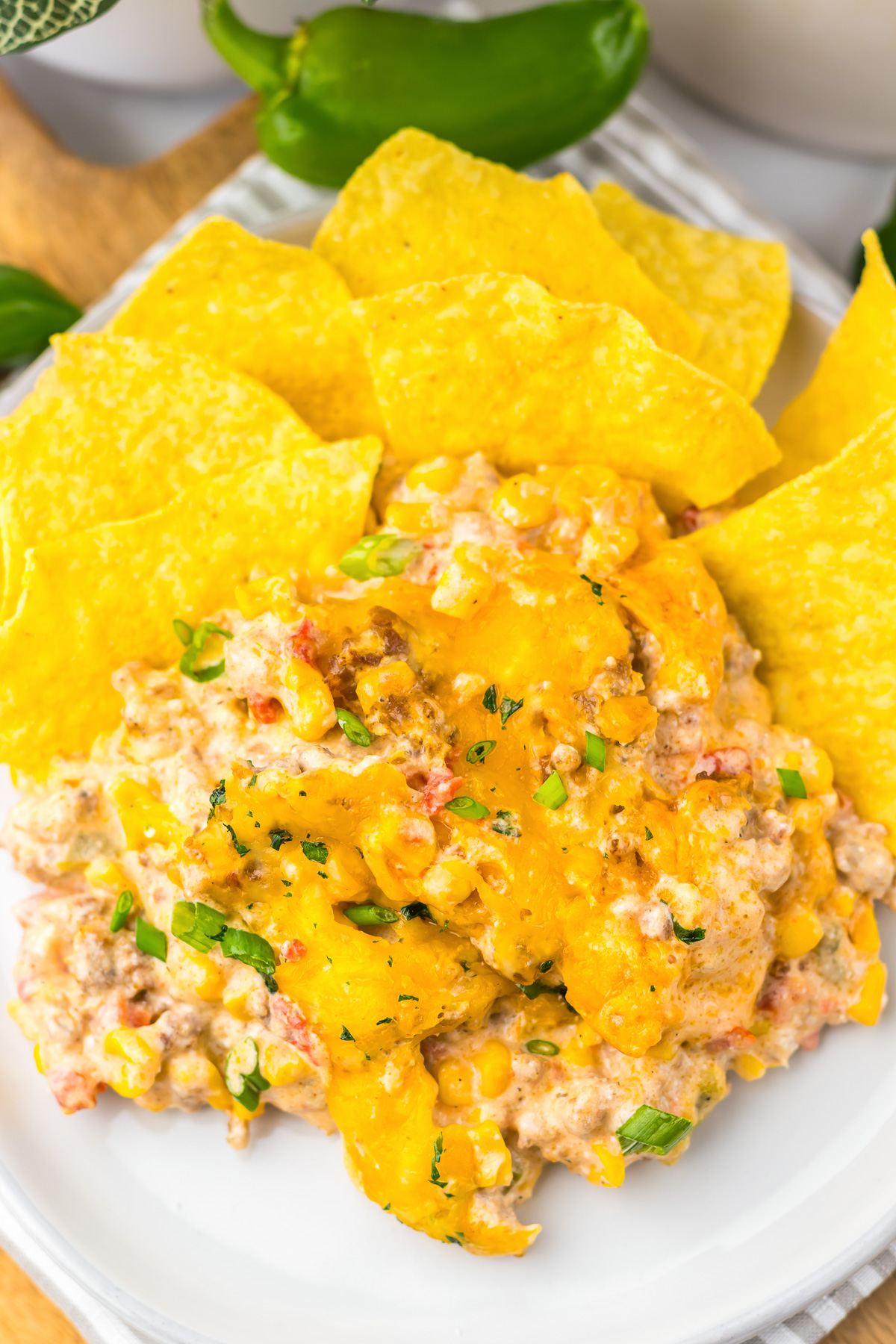 Slow Cooker Cowboy Dip featuring ground beef and cheese, blended with corn, tomatoes, and green onions, served surrounded by yellow tortilla chips on a plate.