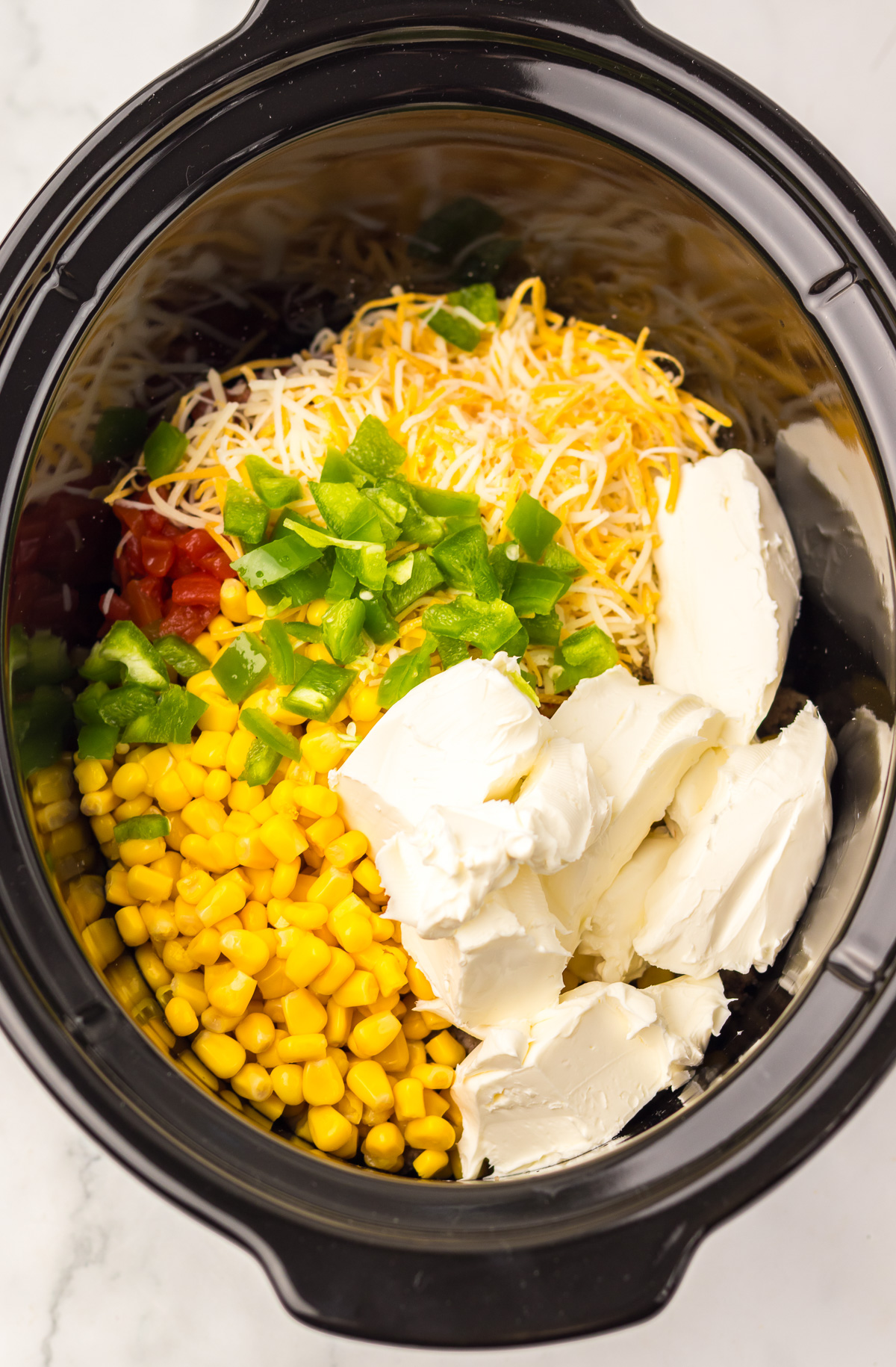 Slow Cooker Cowboy Dip filled with corn, cream cheese, shredded cheese, green peppers, tomatoes, and black beans.