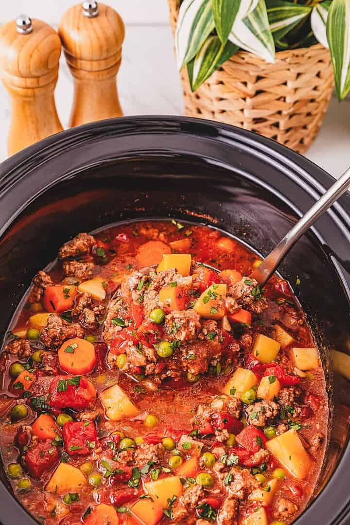 Hearty Crockpot Poor Man&rsquo;s Stew with beef, carrots, peas, and potatoes simmered slowly in a slow cooker, served with a ladle.